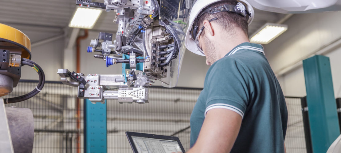 Maschinenbau Ingenieur mit Schutzhelm und Notebook bei der Inbetriebnahme eines Roboters